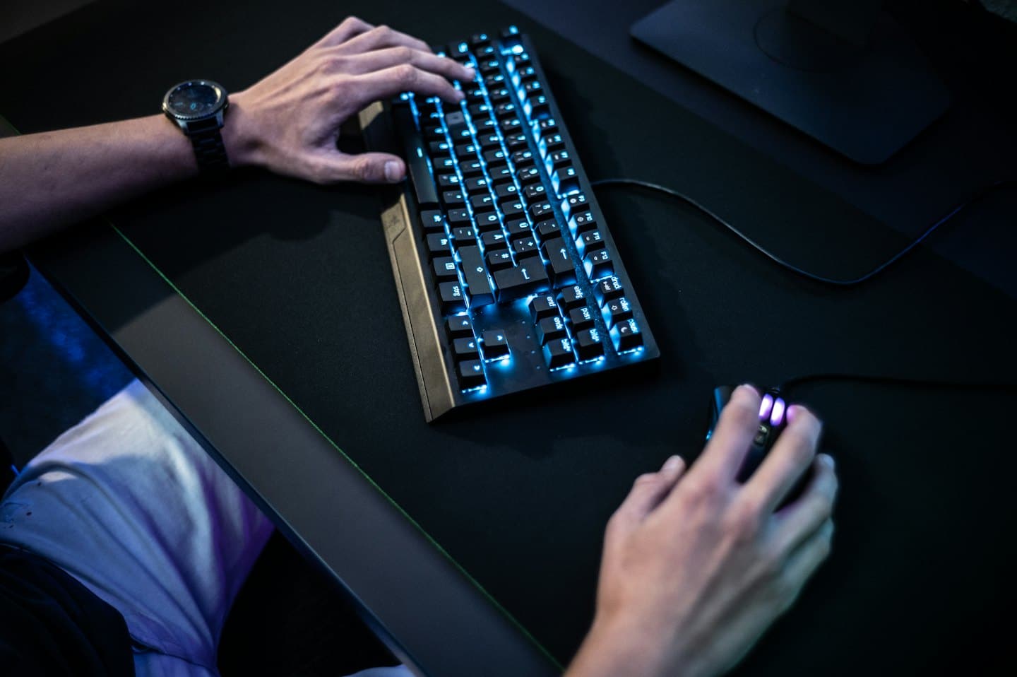 Mani che digitano su una tastiera da gaming blu luminosa e usano un mouse.
