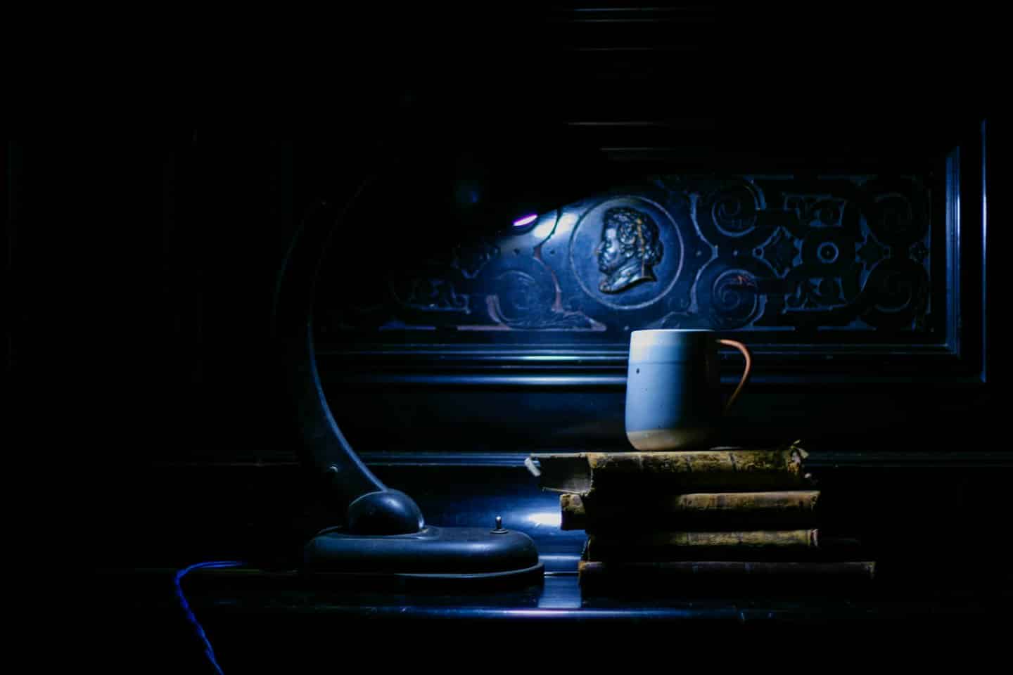 Una lampada antica illumina vecchi libri e una tazza.